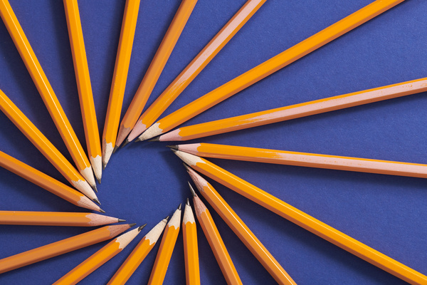 Top view of yellow graphite pencils arranged in a circle on a dark blue surface
