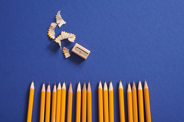 Top view of sharpened yellow graphite pencils and a sharpener on a blue surface
