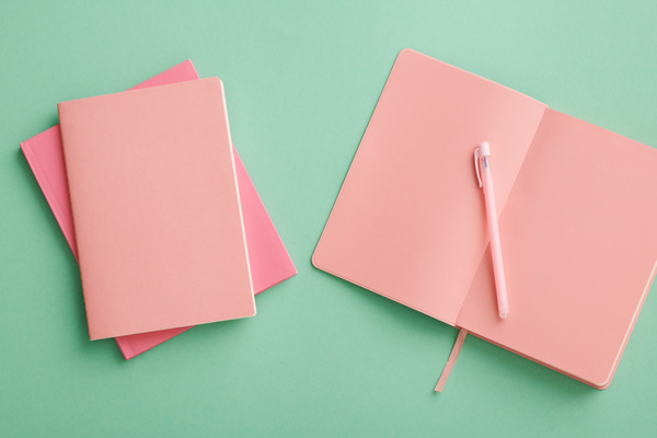 Top view of bright pink notebooks and a pen laid out on a turquoise surface