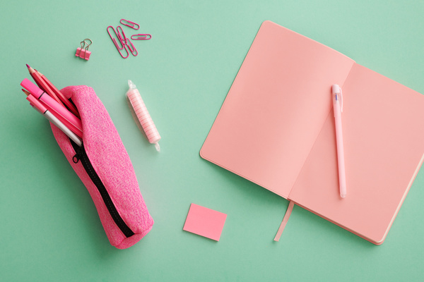 Top view of a set of pink office supplies lying on a turquoise surface