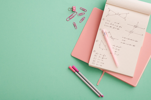 Top view of a school set of pink stationery items and mathematical notes in a notebook lying on a turquoise surface