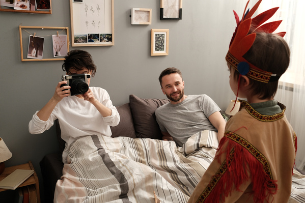 A woman in white clothes photographing her son in an Indian costume while sitting in bed with her husband