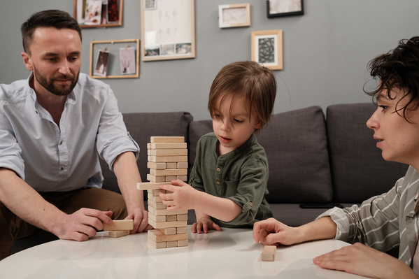 A little boy in a green longsleeve playing jenga with his dark-haired parents