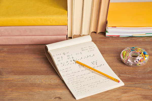 A notebook with study notes and a pencil lying on a wooden table with a holder for paper clips and pins