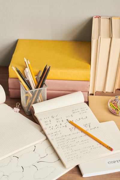 School notebooks with math jottings and a pencil laid out on a wooden table with stationery