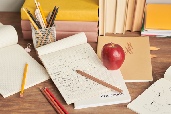 School notebooks on math and a red apple on a wooden desk with stationery