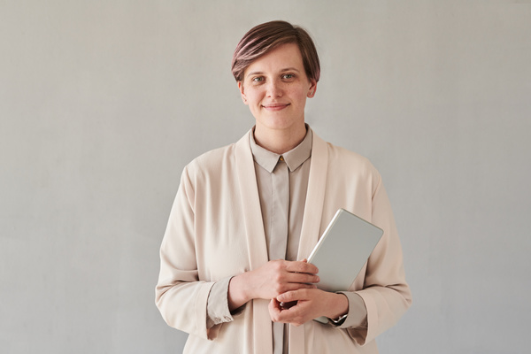 Portrait of a young smiling teacher with short styled hair dressed in an office light suit holding a tablet