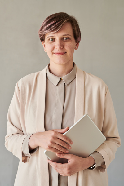 A beautiful teacher with short hair wearing a beige office outfit holding a silver tablet