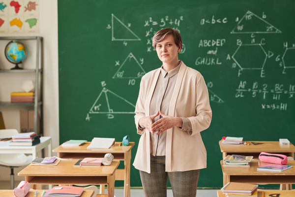 A beautiful educator with short hair wearing a beige suit standing in a school classroom