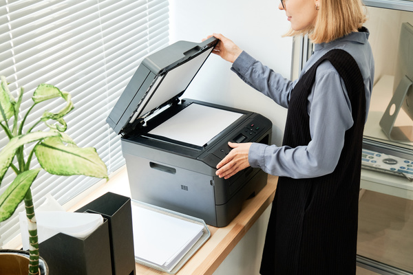 A woman with short blond hair in dark-colored clothes making copies of a document on a copier in the office