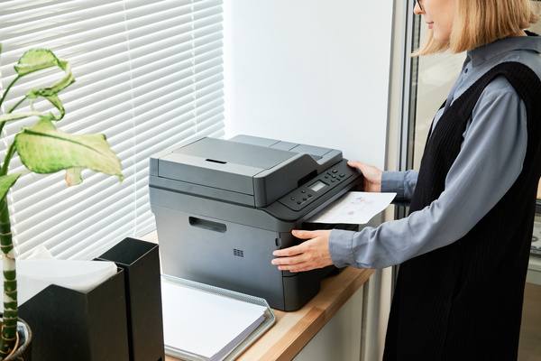A female employee with short blond hair in dark-colored clothes making copies of a document on a copier in the office