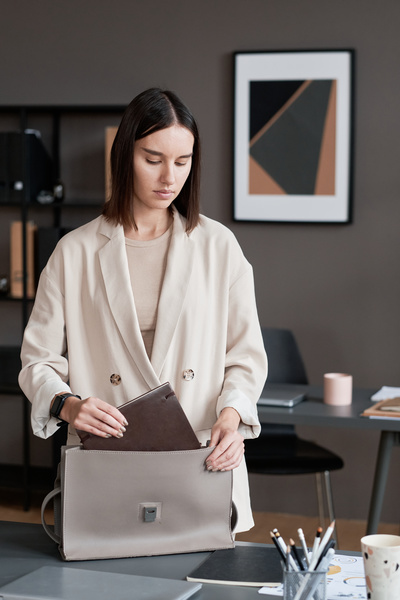 An office worker with short brown hair dressed in light clothes putting a diary in her handbag