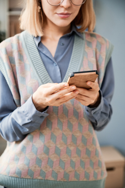 A blonde office worker in a shirt and a knitted sweater vest using a smartphone