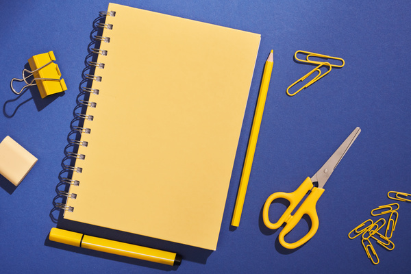 Yellow spiral notebook and stationery on a dark blue matte surface