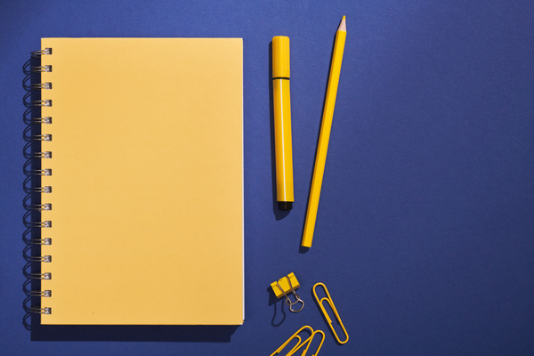 A yellow spiral notebook and a set of stationery lying on a dark blue surface