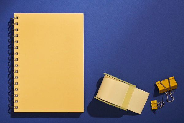 A yellow spiral notepad and stationery items lying on a dark blue surface
