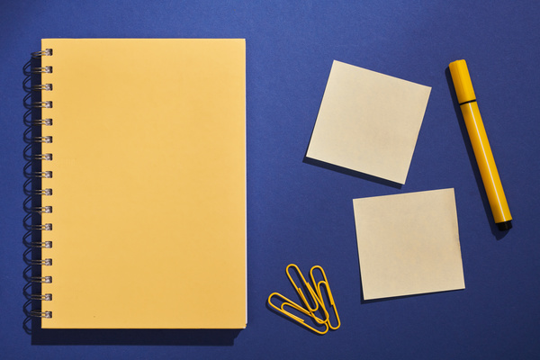 A yellow spiral notepad and office supplies lying on a dark blue surface