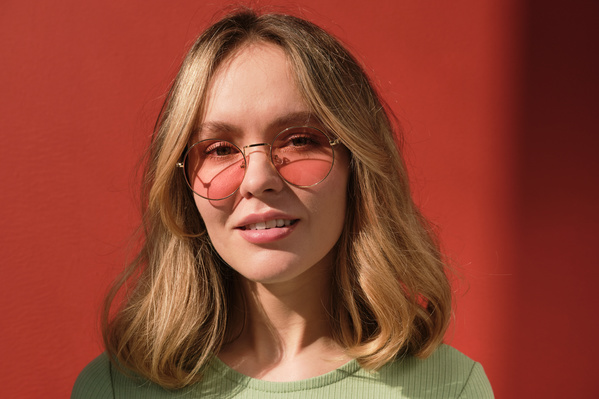 Portrait of a woman with blonde hair wearing sunglasses with red round lenses against a red background