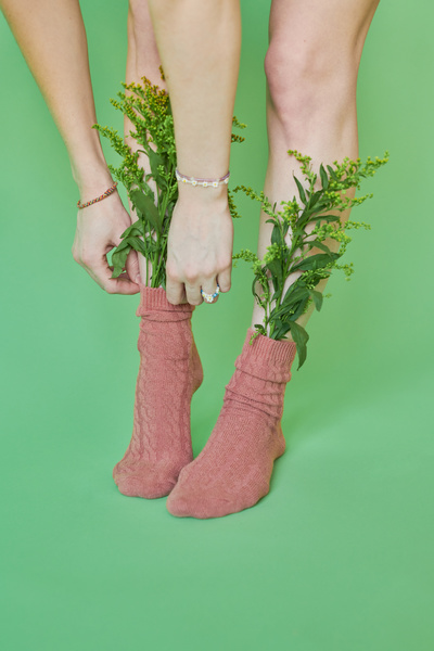 A woman adjusting a pink sock with wildflowers standing against a green background