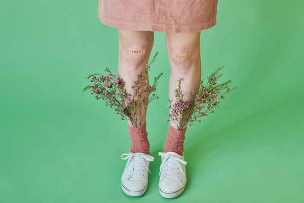 A woman in a light corduroy skirt and white sneakers with wildflowers in her pink socks and stickers with summer inscription on her knees