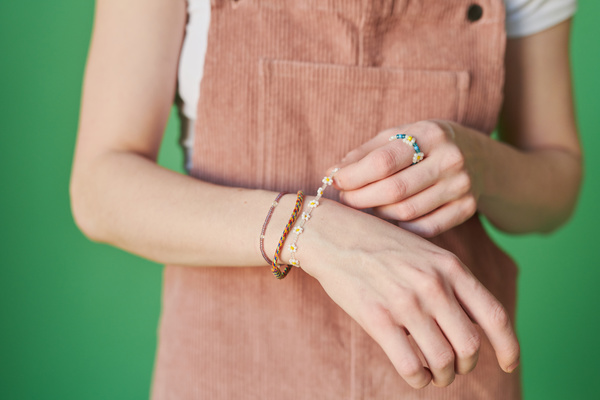 Close-up of multicolored beaded bracelets on the wrists of a woman in a red corduroy sundress