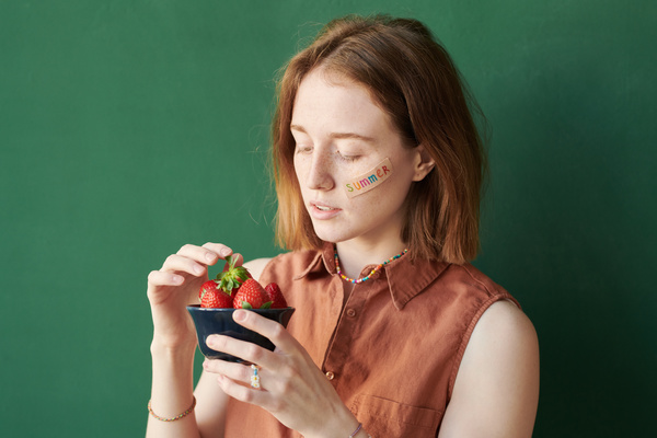 A woman with red hair and a sticker on her face taking strawberries in a black bowl