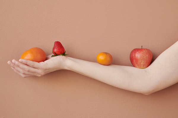 Fruits and berries lying on the arm against a peach-colored wall