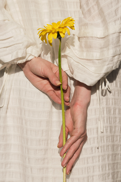 A woman in a white summer dress holding a yellow flower behind her back