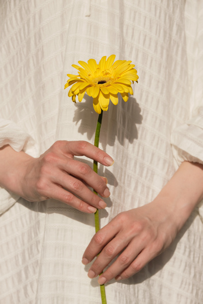Close-up of a yellow flower in the hands of a woman dressed in a white light dress