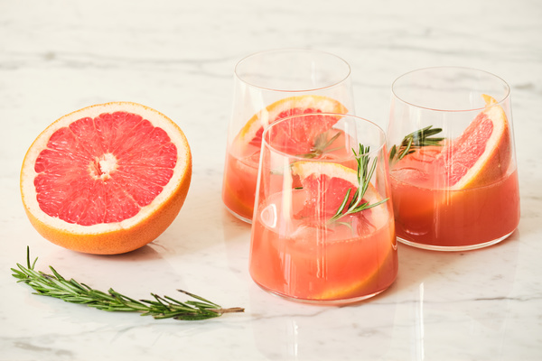 Grapefruit and rosemary cooling drink in glasses on a marble table with its ingredients