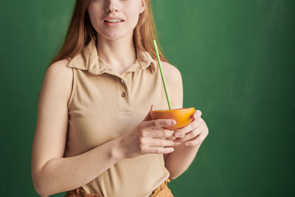 A woman in a beige sleeveless polo shirt holds a half of a grapefruit with a green patterned cocktail straw