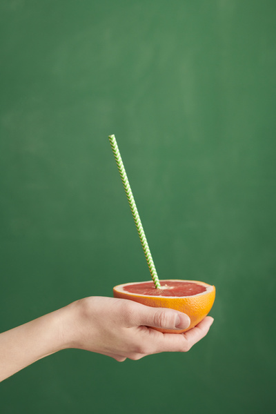 Half a grapefruit with a green cocktail straw with a pattern in the hand against a green background