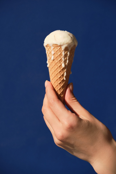 Vanilla melting ice cream in a cone in the hand against a blue background