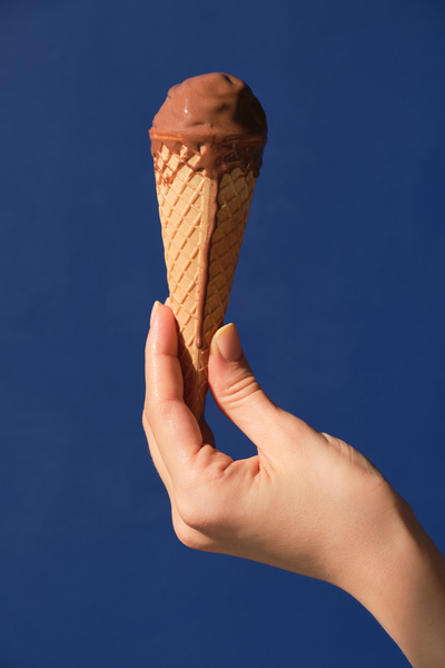 A woman holding chocolate melting ice cream cone against a blue background