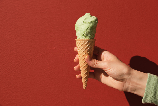 Pistachio melting ice cream in a cone in a womans hand against a red background