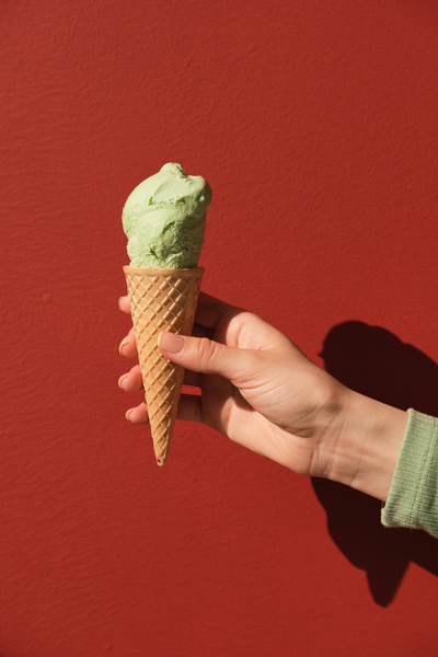 A ball of pistachio ice cream in a cone in female hand against a red background
