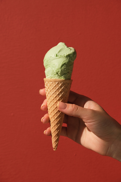 A portion of pistachio ice cream in a cone in a womans hand against a red background