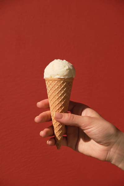 Vanilla ice cream cone is held in a hand against a red background