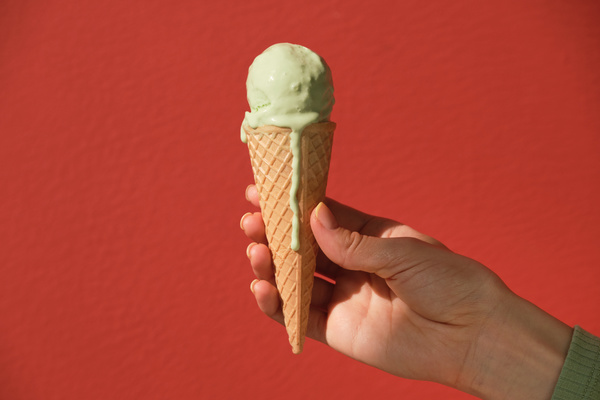 Melting pistachio ice cream in a cone held in a hand against a red background