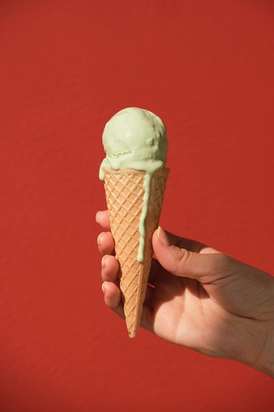 Melting pistachio-flavored ice cream in a cone in a hand on a red background