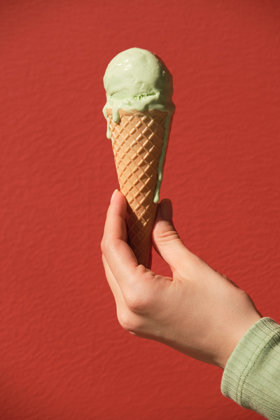 Melted ice cream in a cone with pistachio-flavor in the left hand on a red background