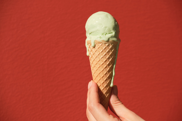 Close-up of melted pistachio-flavored ice cream in a cone in the left hand on a red background