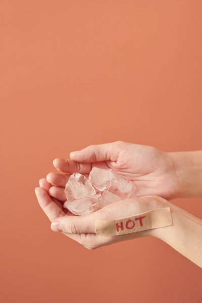 Melted pieces of ice in the hands with a sticker with the inscription hot on a bright blurry background