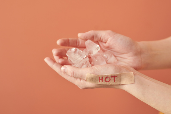Close-up of melting ice pieces in hands with a sticker with a red inscription on a coral blurred background