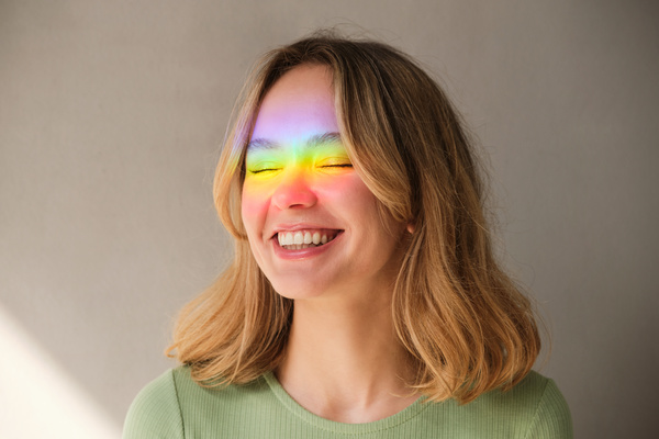 Portrait of a smiling woman with short blonde hair and closing her eyes and her face highlighted by a rainbow ray
