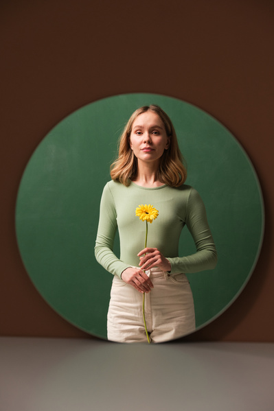 Mirror reflection of a woman in a light outfit with light short hair with yellow gerbera