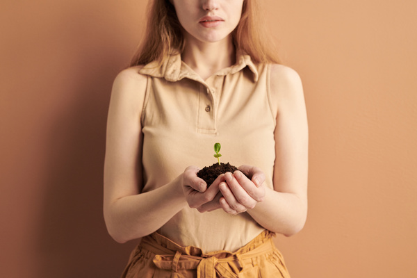 A handful of earth with a sprout in the hands of a woman in a beige outfit