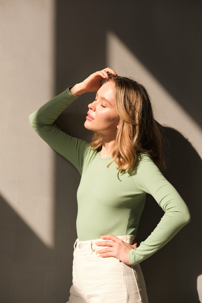 A woman with short blonde hair with her eyes closed posing in a sunlit space