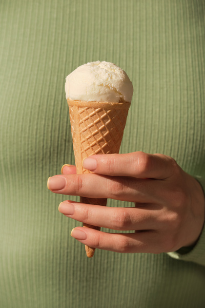 A woman dressed in a green longsleeve holding a vanilla-flavored ice cream in a cone