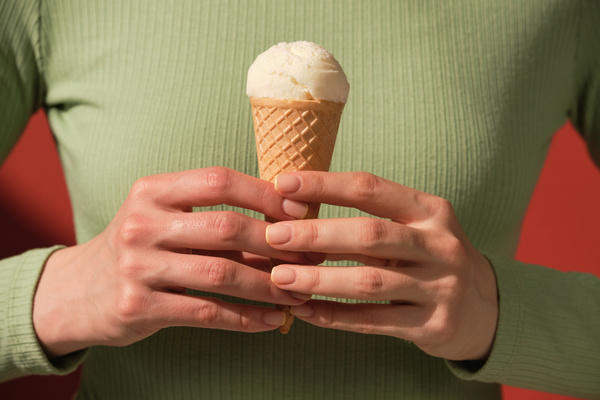 A woman in a green longsleeve holding a vanilla ice cream cone in her hands